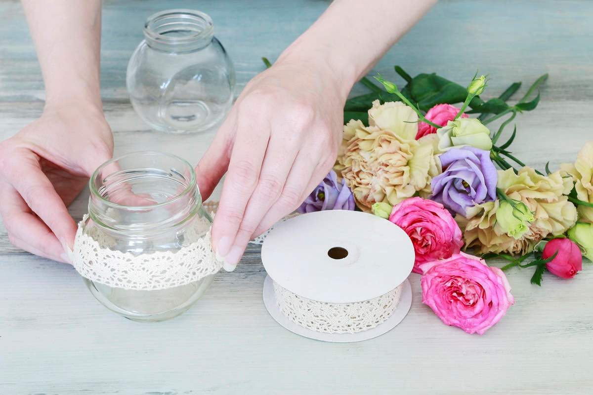 Decorating a clear glass mason jar with white lace.