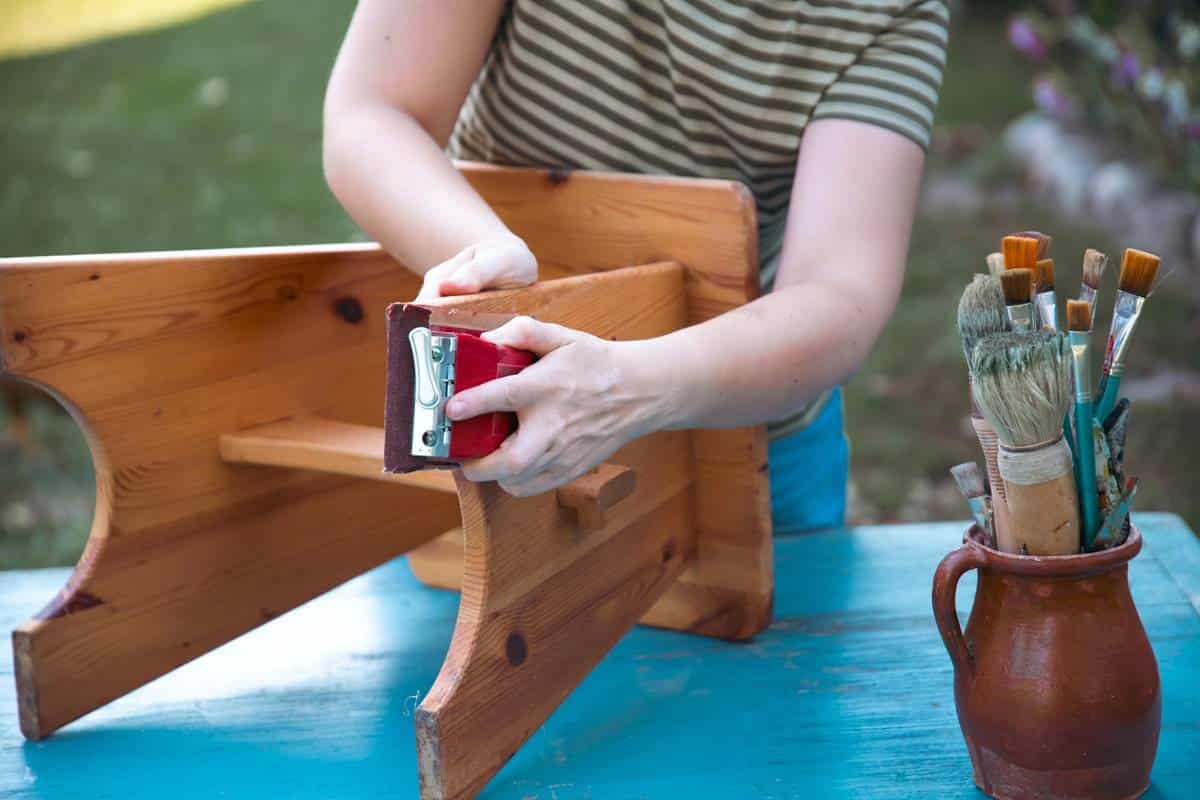 Person sanding a wooden bench on a blue table.