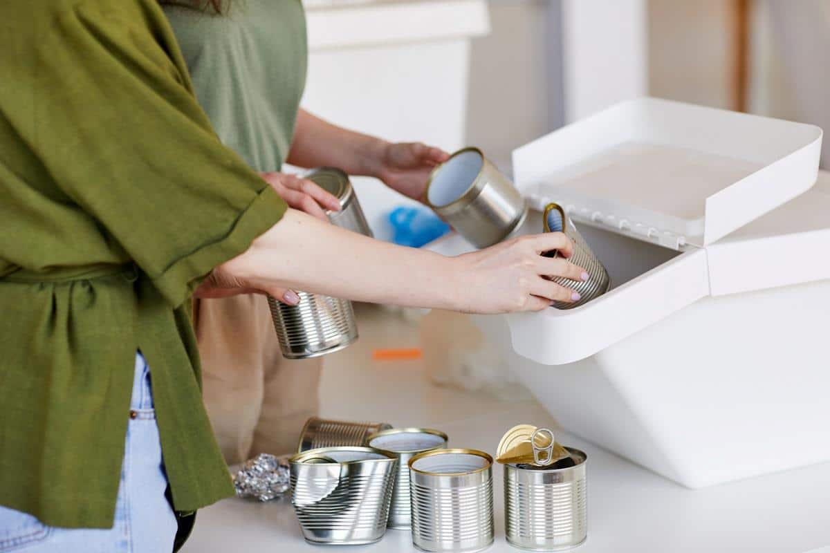 Thoughtfully sorting empty tin cans near a recycling bin.